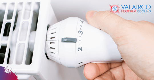 A hand turning the dial on a white radiator